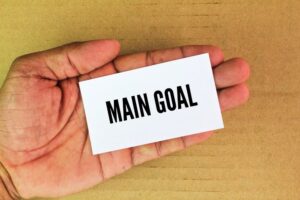 Hand holding a white paper with the words 'Main Goal,' symbolizing the primary or most important objective that an individual, team, or organization aims to achieve.