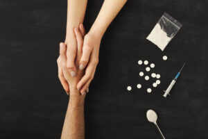 Drug addict hands asking for help on dark table with cooked heroine, pills, spoon and plastic bag. Concept for drug addiction and International Day against Drug Abuse, top view