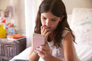 Young Girl In Bedroom Worried By Bullying Text Message