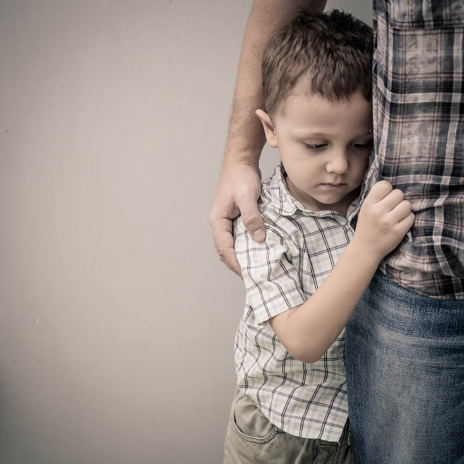 Child looks sad and grabs a man's leg, and the man's arm is around the child's back. In Florida, child abuse must be reported by mandatory reporters