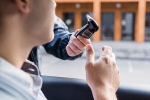 Cropped view of a police officer handing a breathalyzer device to a driver seated in a car, with the foreground blurred for emphasis.