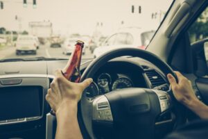 Driver holding an alcoholic bottle while driving, illustrating the dangers of drunk driving.