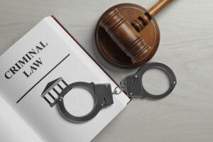 Judge's gavel, handcuffs, and a criminal law book arranged on a white wooden background, symbolizing justice and legal matters.