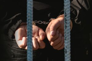 Man in handcuffs standing behind bars in a police station, symbolizing imprisonment and the prisoner concept.