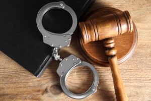 Flat lay of a book, judge's gavel, and handcuffs on a wooden table.